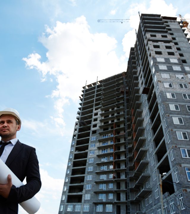Elegant investor in helmet talking on mobile phone by unfinished building